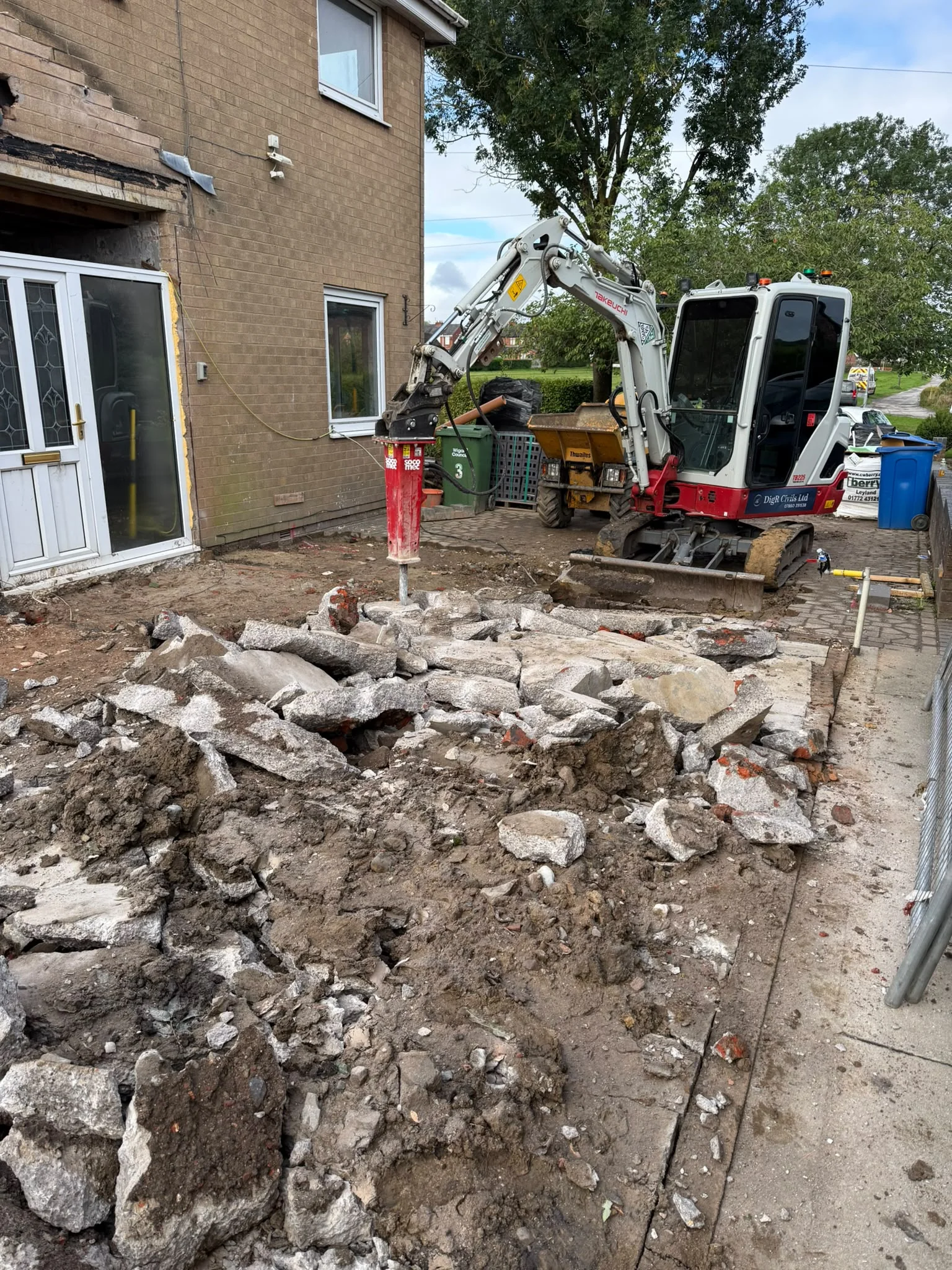 Hydraulic breaker working against concrete beside a house