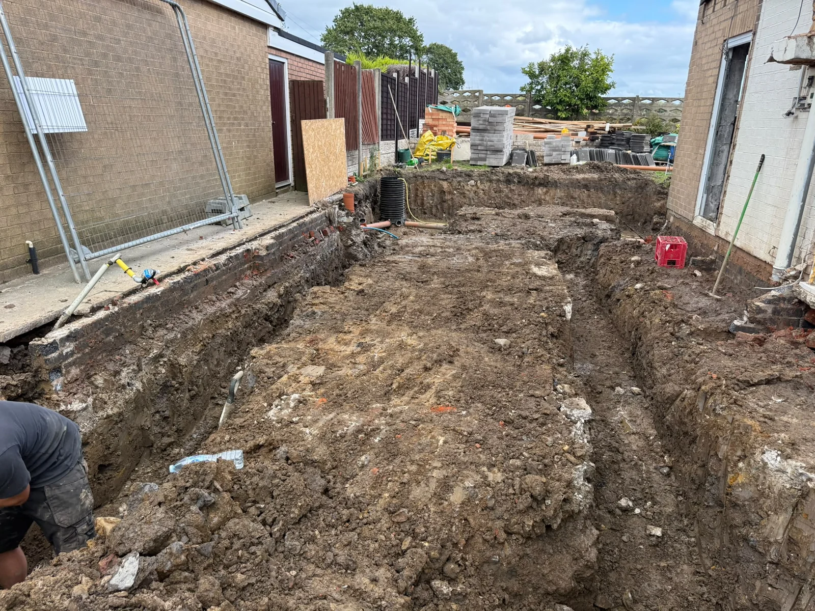 Excavator completing a deep foundation excavation beside a house